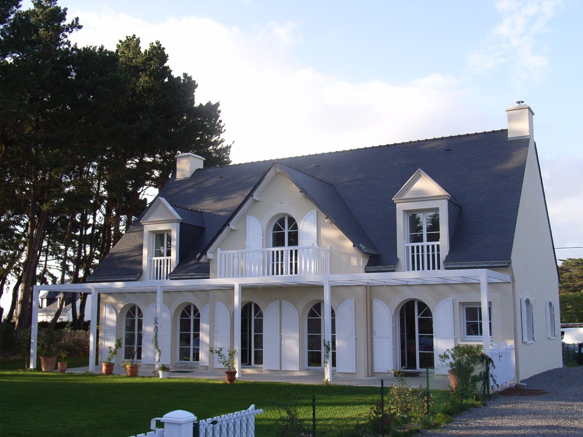 Grande maison avec toiture en ardoise et fenêtres avec grands volets en bois blanc